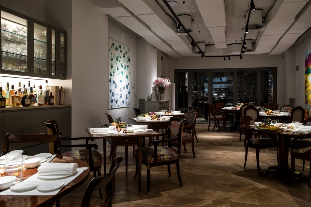 Muestra un espacio del Restaurante Pabu, donde se aprecian 7 mesas y en el fondo de la sala se ve una cristalera con una bodega